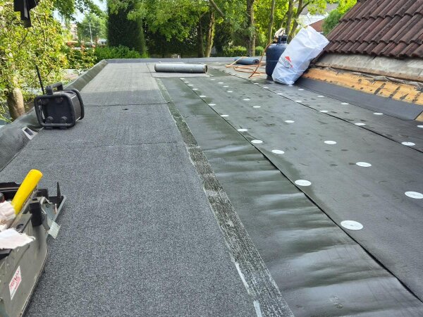 Plat dak halverwege: links de afgewerkte toplaag, rechts de onderlaag vastgezet met ringen
